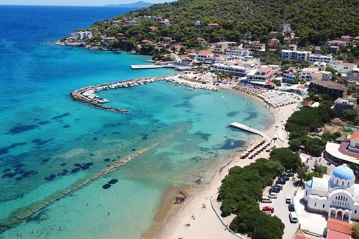 Agistri’s Skala waterfront, with a curved beach, village buildings and a blue-domed church