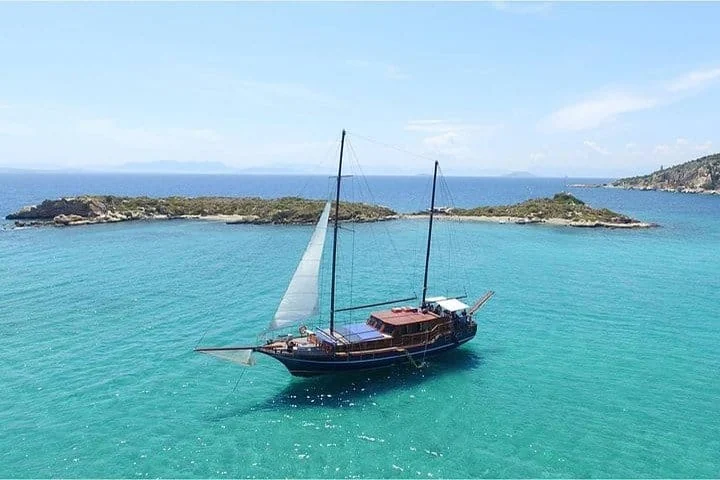 Wooden sailing boat in pale turquoise water beside a low rocky island