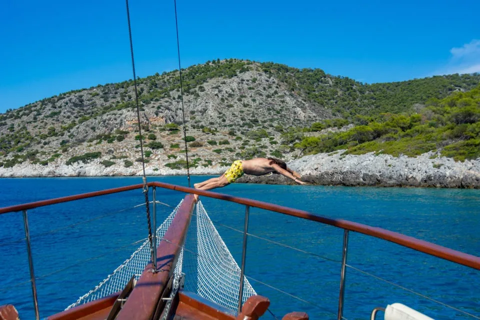 A guest diving off the bow into clear water beside a rocky islet