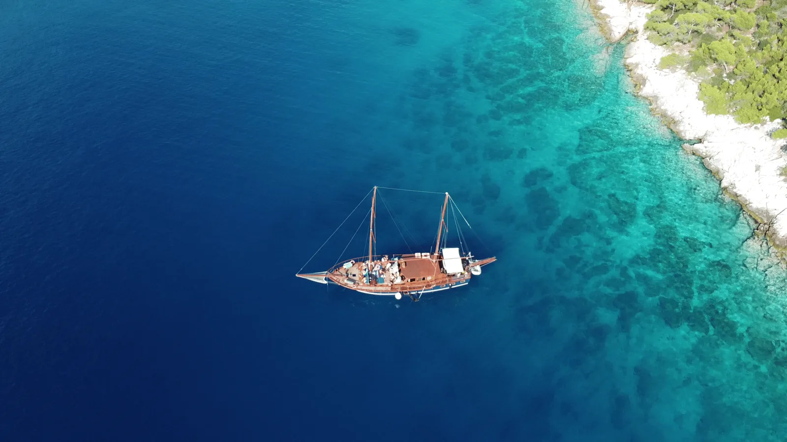 A wooden cruise boat beside the blue and turquoise Saronic coast