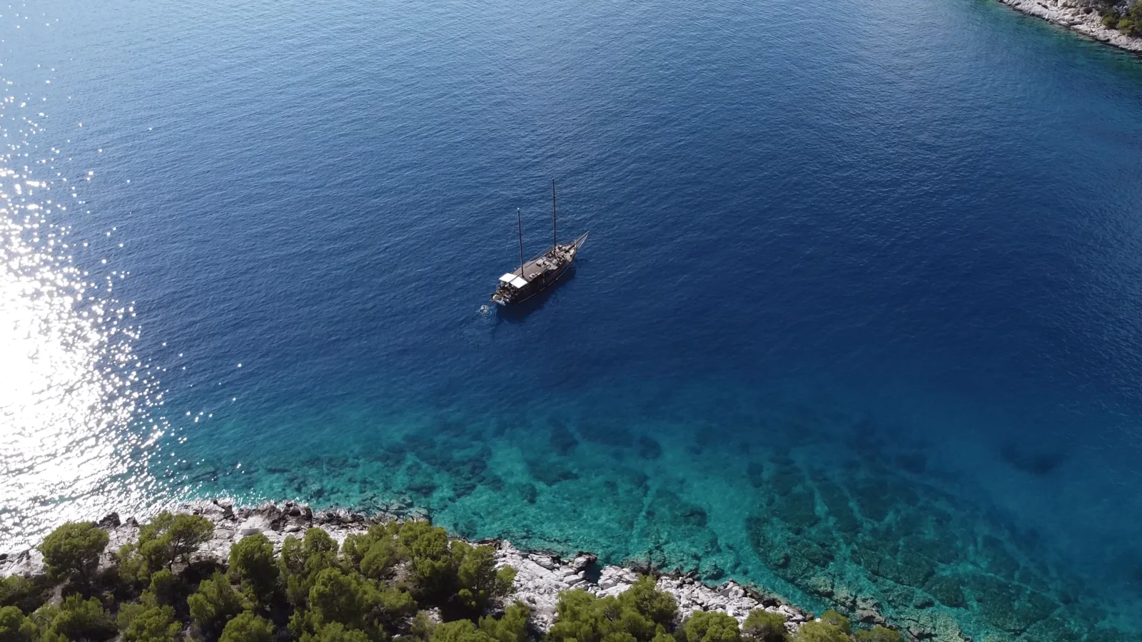 Blue water, a wooded shoreline and a wooden boat seen from above